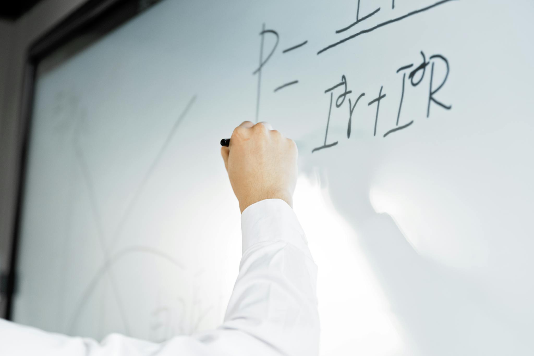 Close-up of a hand writing a formula on a whiteboard in a professional setting.