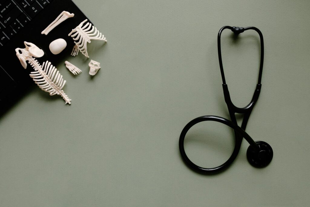 A flat lay of medical tools and small skeleton models on a green desk.