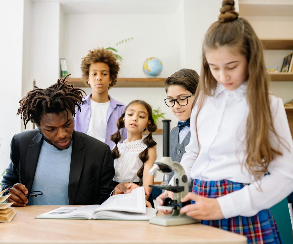 A teacher and students in a classroom engaging with a microscope for a science lesson.