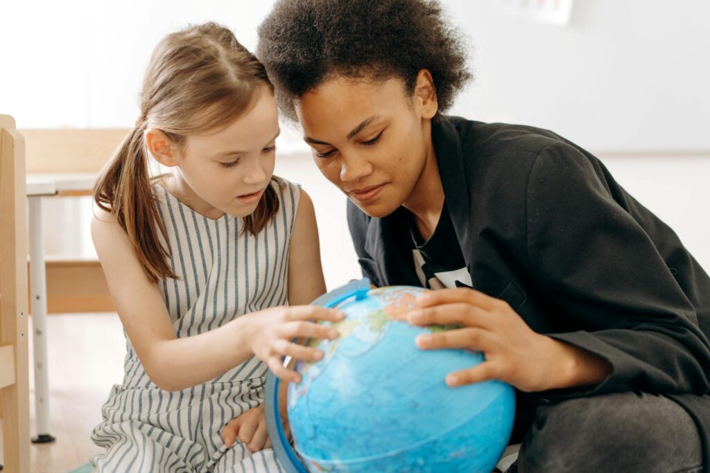 Child and teacher exploring a globe, symbolizing education and knowledge.