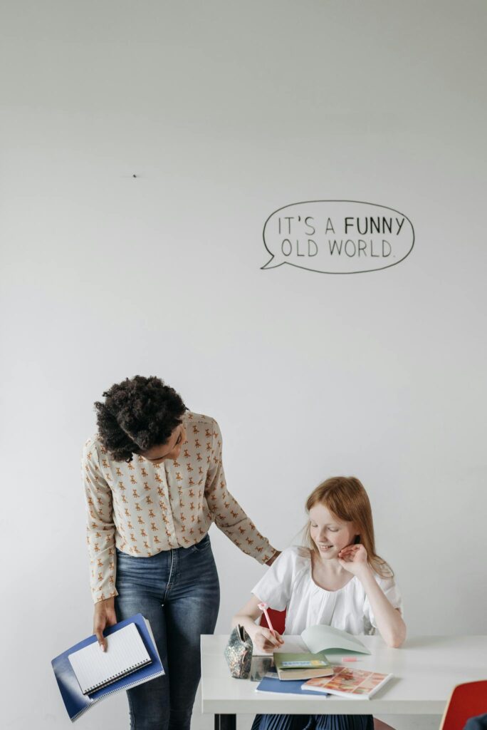 Teacher helping a student in a classroom setting, encouraging learning with personalized attention.